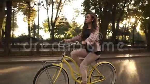 在夏季城市公园的街道或林荫大道上骑自行车的头发很长的女孩穿着粉色休闲服视频的预览图
