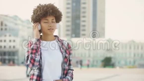 戴着耳机听着最喜欢的歌在户外唱歌的年轻女性视频的预览图