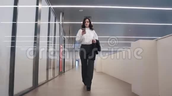 自信的商务女性使用手机穿着西装的女孩穿过办公楼视频的预览图