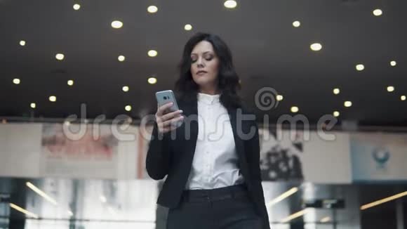 一位手里拿着智能手机的女商人正走在一座现代化办公楼的大厅里一个女孩的肖像视频的预览图