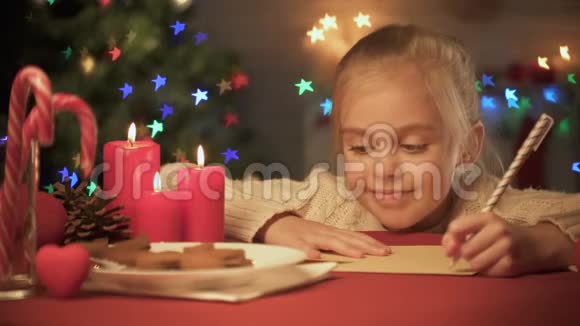 可爱的女孩为圣诞老人写信在圣诞节装饰的桌子上愿望清单视频的预览图