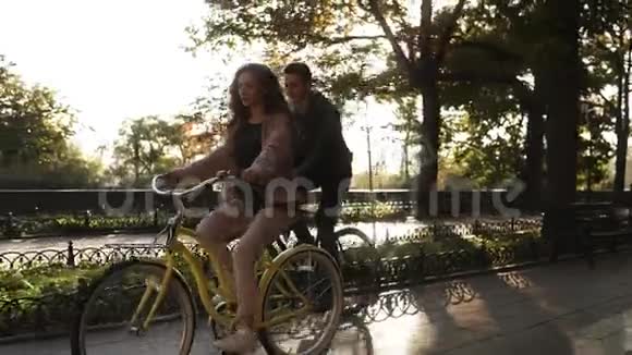 美丽的年轻夫妇在空荡荡的城市公园里骑自行车停下来坐在长凳上拥抱可爱的一对视频的预览图