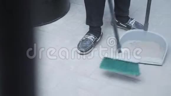 有人穿着运动鞋把白色地板上的碎片扫到簸箕里视频的预览图