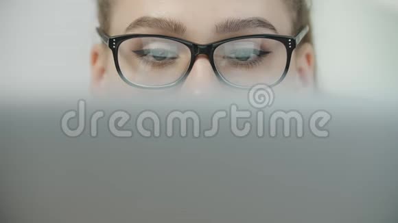 眼睛疲劳戴眼镜的十几岁的学生女孩用笔记本电脑在笔记本上打字准备考试视频的预览图
