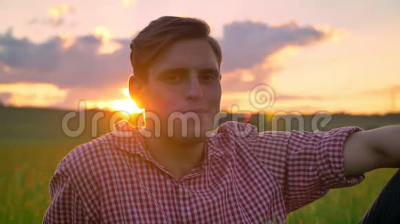 美丽的年轻人微笑着看着摄像机坐在麦田里背景是夕阳大自然令人惊叹视频的预览图