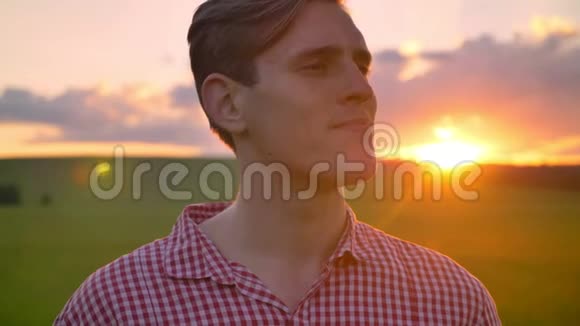 年轻英俊的男子转过头看着镜头微笑着美丽的绿野与日落视频的预览图