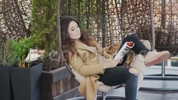 一个穿着毛衣和外套的漂亮女孩正坐在咖啡馆的椅子上在电话里情绪化地交谈视频的预览图