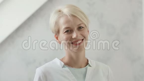 年轻微笑的女人穿着白色实验室外套的金发美容师视频的预览图