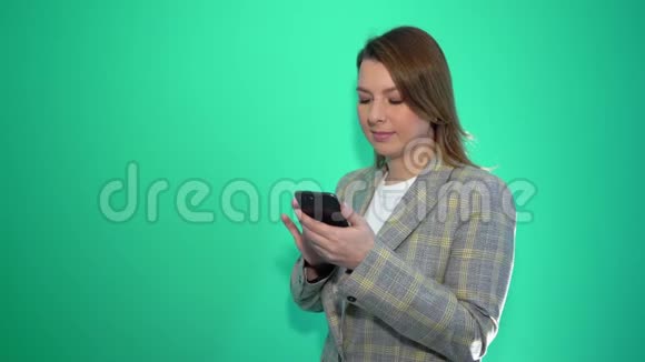 惊讶的金发女孩在手机上发短信而站在绿色的背景上视频的预览图
