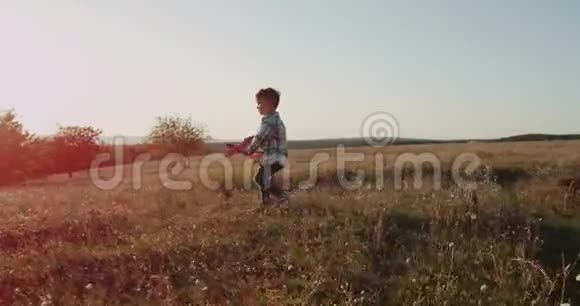 微笑的小男孩玩着飞机在田野的中央快乐地跳跃美丽的日落视频的预览图