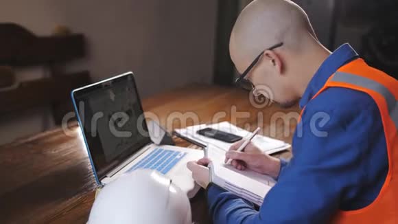 男工程师在房间里为一台穿着工作服的笔记本电脑工作安全帽躺在桌子上视频的预览图