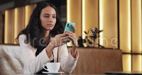 商务女性穿着粉色西装使用智能手机在舒适的咖啡厅喝咖啡视频的预览图