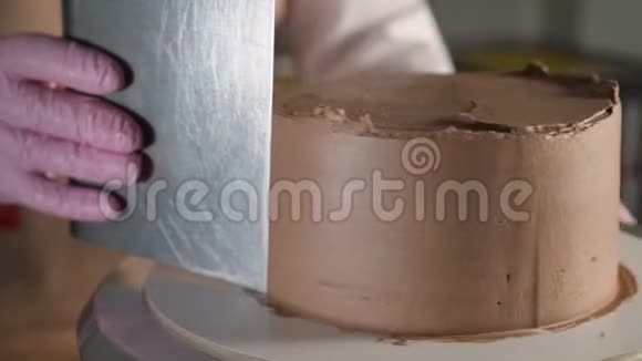 糕点厨师女士正在烘焙室的旋转蛋糕架上用金属刮刀在海绵蛋糕上涂抹巧克力奶油视频的预览图