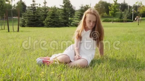 伤心的小女孩坐在草地上低头看阳光明媚的夏日视频的预览图