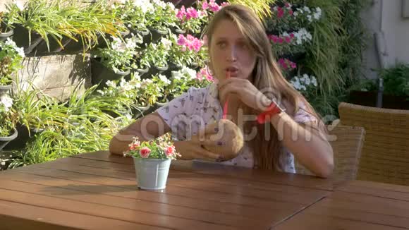年轻女子端着椰子饮料坐在桌旁视频的预览图