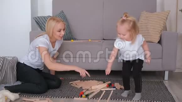 可爱的金发小女孩和妈妈坐在沙发边玩木块建造这座塔并把它弄坏视频的预览图
