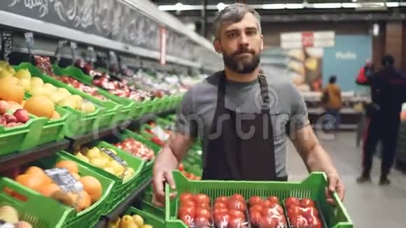 水果和蔬菜部超市里一个年轻的推销员穿着围裙背着一盒西红柿视频的预览图