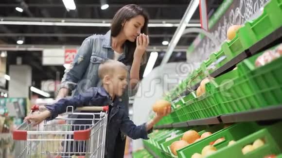 年轻的女人和她的儿子正在挑选水果他们从塑料盒子里拿水果然后闻闻它们视频的预览图