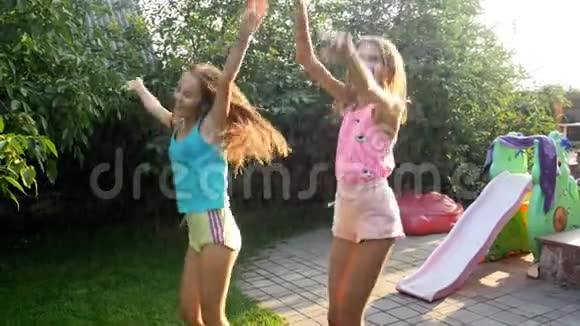 4k视频两个快乐欢笑的少女在花园水管喷水下跳舞视频的预览图