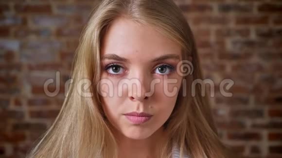 年轻愤怒的白种人金发女郎看着镜头肖像背景中的砖墙视频的预览图