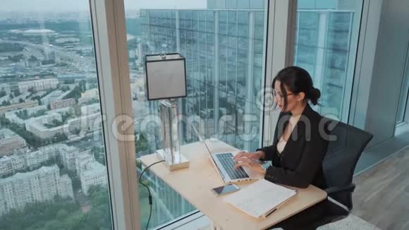 年轻的商务女性在一个位于摩天大楼高层的现代办公室里用笔记本电脑工作视频的预览图