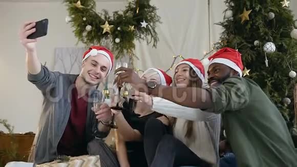 戴着圣诞老人帽子戴着酒杯的快乐男女在靠近智能手机的智能手机上自拍视频的预览图
