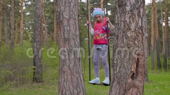 快乐的少年女孩在春日公园的松树间荡秋千视频的预览图