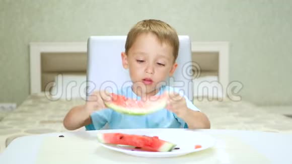 一个可爱快乐的孩子坐在厨房的桌子旁正在吃一个有食欲的多汁的西瓜视频的预览图