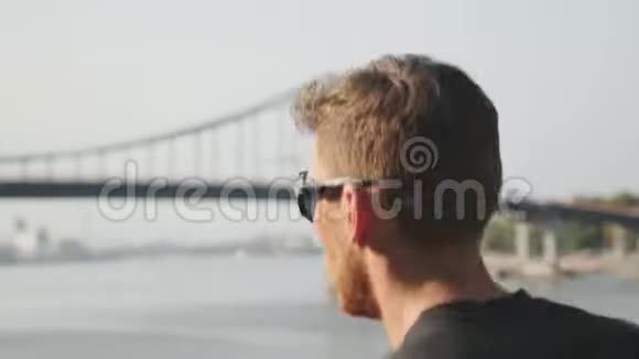 活泼苗条的男人沿着河跑年轻的肌肉男在桥附近跑步在城市慢跑时精力充沛的跑步者视频的预览图