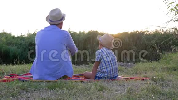 一家人闲着爸爸带着儿子戴着草帽在日落的背景下躺在毯子上在露天的乡村视频的预览图