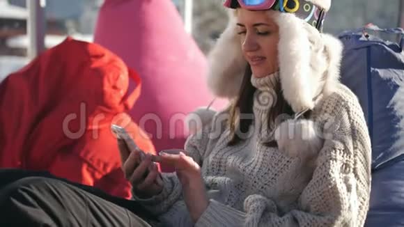 一个女孩用智能手机坐在滑雪场的咖啡馆里年轻女子在高山滑雪场放松视频的预览图