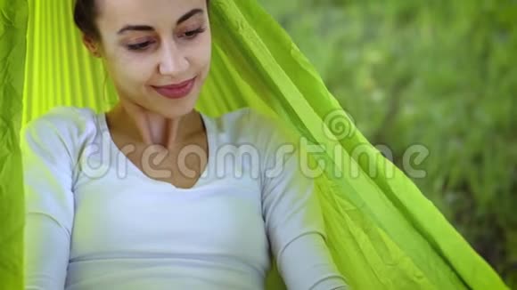 迷人的年轻女子与可爱的威尔士科尔吉狗躺在明亮的绿色吊床在公园和阅读一本书视频的预览图