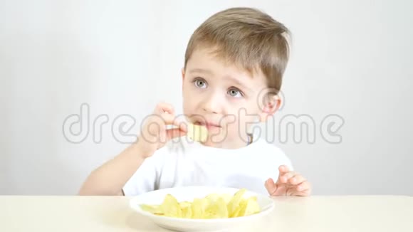 一个喜欢吃白色盘子里的薯片的孩子坐在白色背景的桌子上视频的预览图