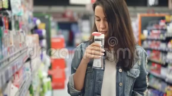 年轻的女人在超市买化妆品她打开瓶子里的液体闻着它然后微笑着视频的预览图