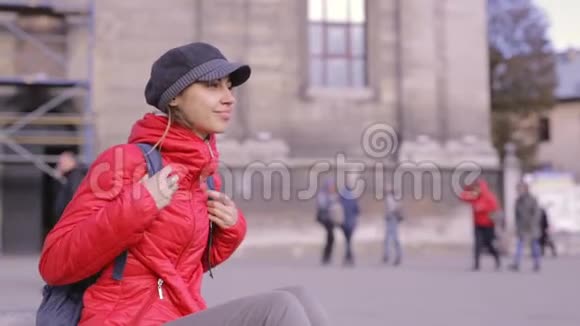 穿着红色夹克和灰色帽子的年轻女子坐在街上视频的预览图