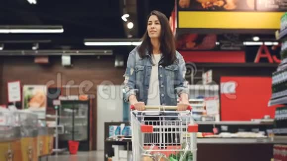 穿着休闲装的漂亮女士走在杂货店里手里拿着食物的购物车看上去很漂亮视频的预览图
