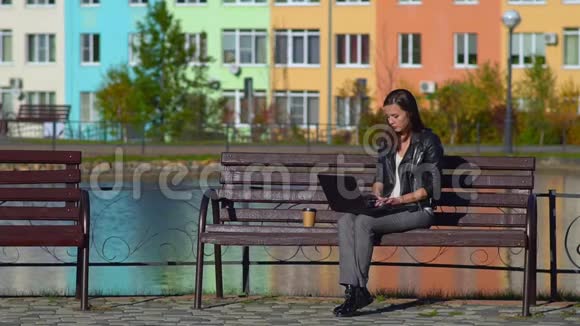 公园里的女孩坐在长凳上用笔记本电脑工作她感冒了用手帕擦鼻子视频的预览图