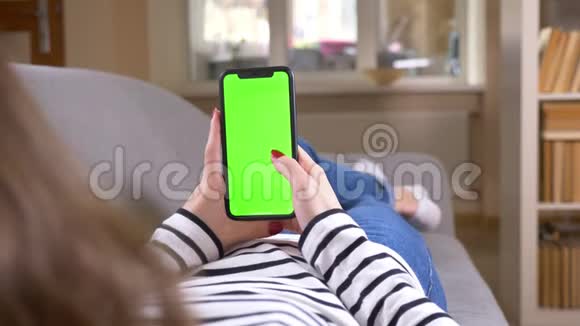 女性使用绿色屏幕手机的特写后视图拍摄手机垂直放置在室内沙发上视频的预览图