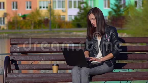 公园里坐在长凳上在笔记本电脑里工作的女孩她感冒了用手帕擦鼻子视频的预览图
