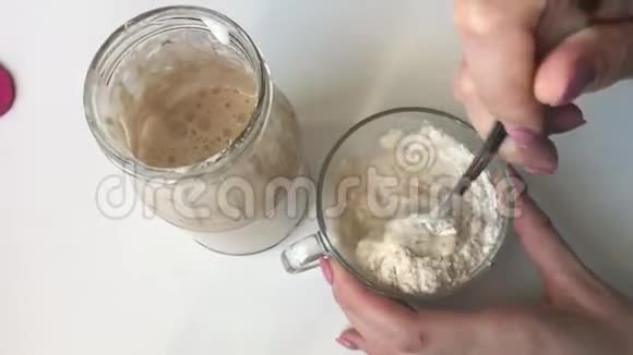 一个女人正在把面粉和水混合在玻璃杯里使面包变酸的混合物酸面包立在一个玻璃罐子旁边视频的预览图