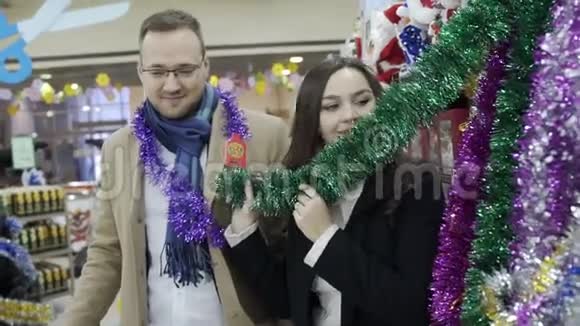 年轻的微笑家庭在购物中心选择圣诞树的装饰视频的预览图