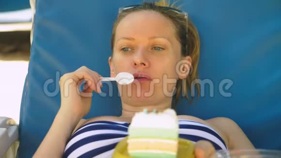 穿着泳衣的女人躺在海边的休息室里吃蛋糕视频的预览图