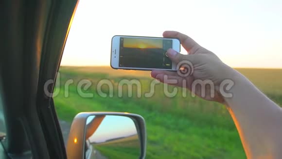 男人手在日落时在手机智能手机上拍照一个人在阳光下从车窗手阳光照射着视频的预览图