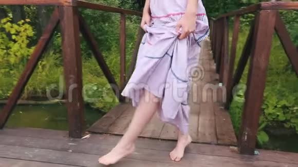 一个漂亮的年轻女子的特写镜头她的腿穿着轻盈的裙子走在河边的一个木墩上乡村散步视频的预览图