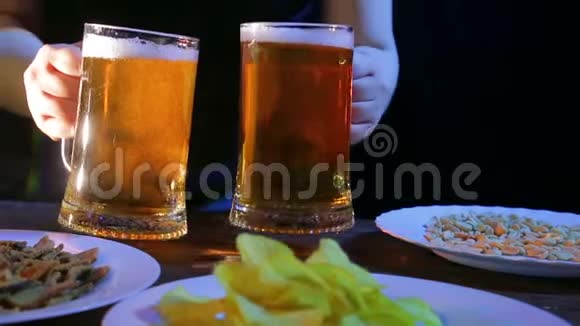 一个女酒保在一张桌子上放着黑色背景的零食两个装满泡沫啤酒的杯子视频的预览图