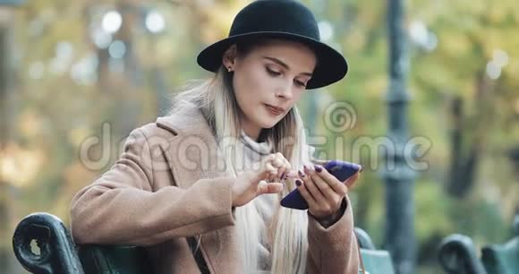快乐的年轻女性使用智能手机语音识别功能她坐在秋公园的长椅上发号施令视频的预览图