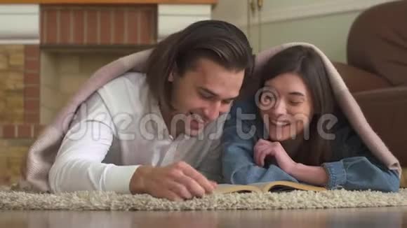 快乐的年轻人和女孩躺在地板上的地毯上读一本书视频的预览图