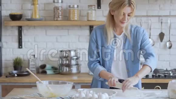 迷人的金发女人35岁在厨房里煮面团女人卷披萨面团慢动作视频的预览图