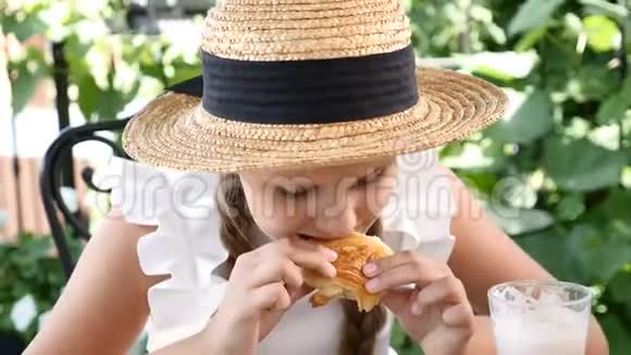 一幅可爱的小女孩戴着草帽在街头咖啡馆里吃饭的肖像她吃奶酪牛角面包微笑着视频的预览图