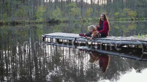 美丽时尚的母子坐在公园湖边的桥上欣赏秋天的风景视频的预览图